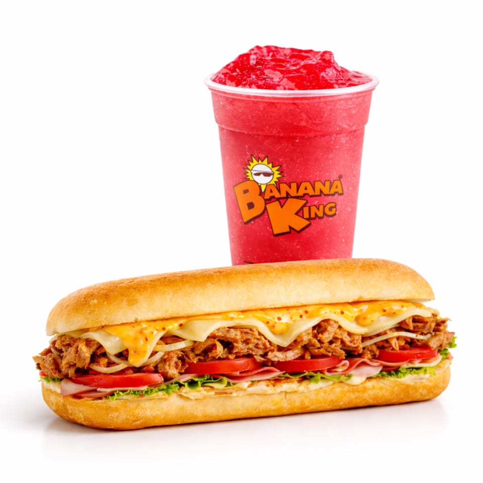 Banana King sandwich with shredded meat, melted cheese, ham, tomatoes, lettuce, and onions beside a red frozen drink.