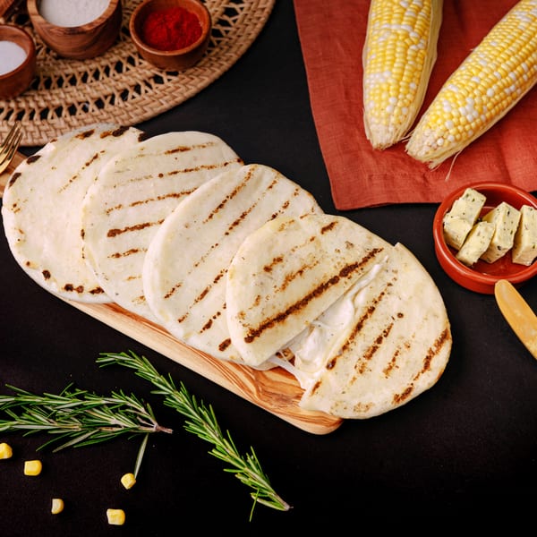 Grilled arepas with melted cheese, corn, rosemary, and spices on a dark surface.