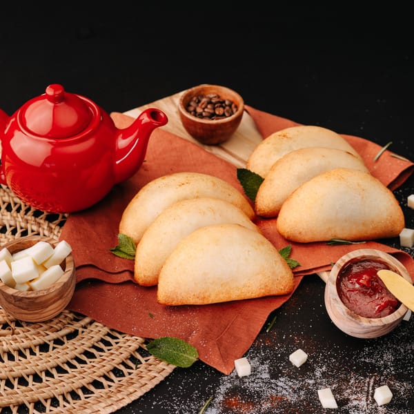 Golden empanadas on an orange napkin with a red teapot, coffee beans, sugar, and jam.
