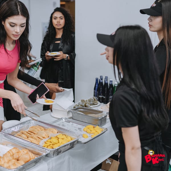People serving themselves fast-food items like empanadas and plantains from a buffet table.