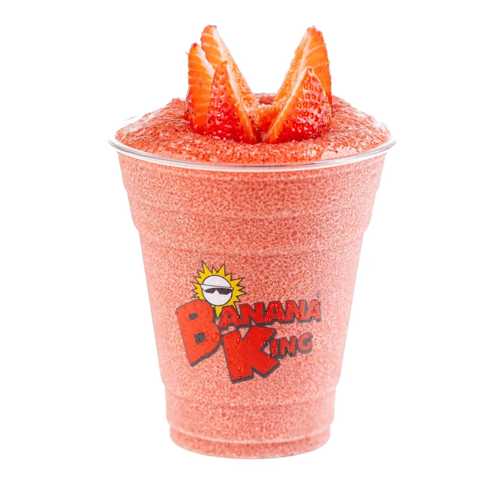 A Banana King strawberry smoothie in a clear cup, topped with fresh strawberry slices.