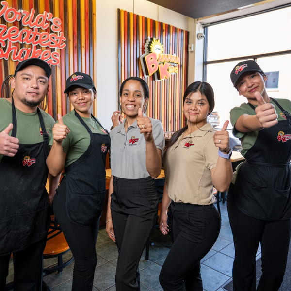 Five Banana King employees, including a manager and cashier, smiling and giving thumbs up in the restaurant.