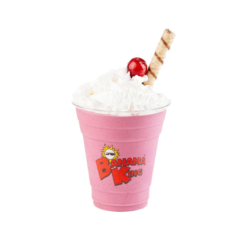 Pink Banana King smoothie topped with whipped cream, a red cherry, and a wafer stick.