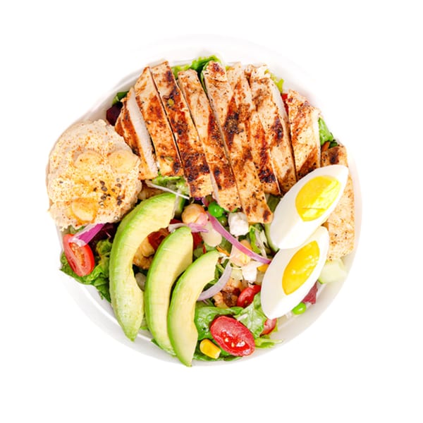 Overhead view of a salad with sliced grilled chicken, avocado, hard-boiled eggs, and hummus.