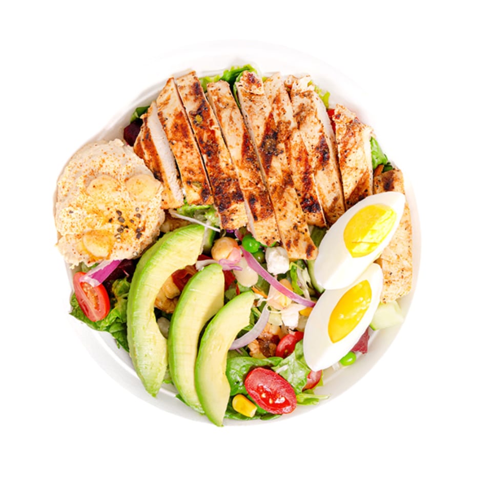Overhead view of a salad with sliced grilled chicken, avocado, hard-boiled eggs, and hummus.