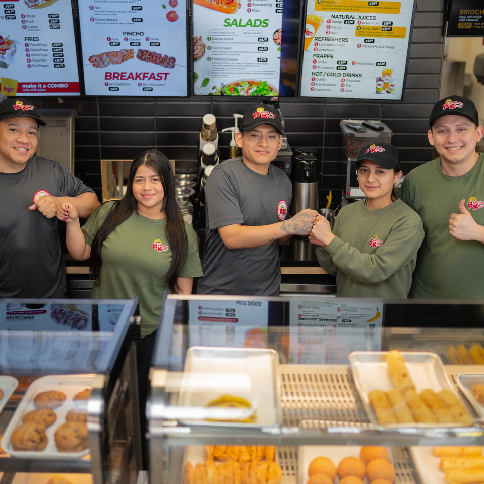 Five Banana King employees in uniform pose behind a counter with menu boards and food displays.