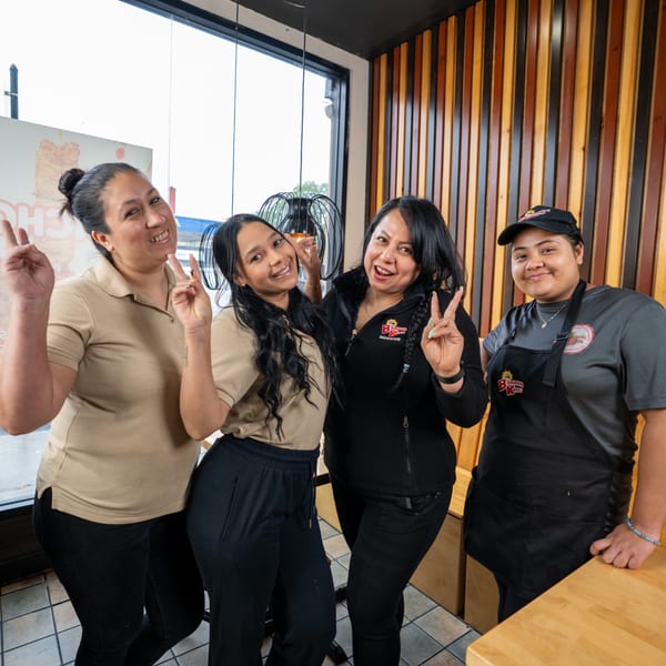 Four smiling Banana King restaurant employees pose together, making peace signs at the camera.