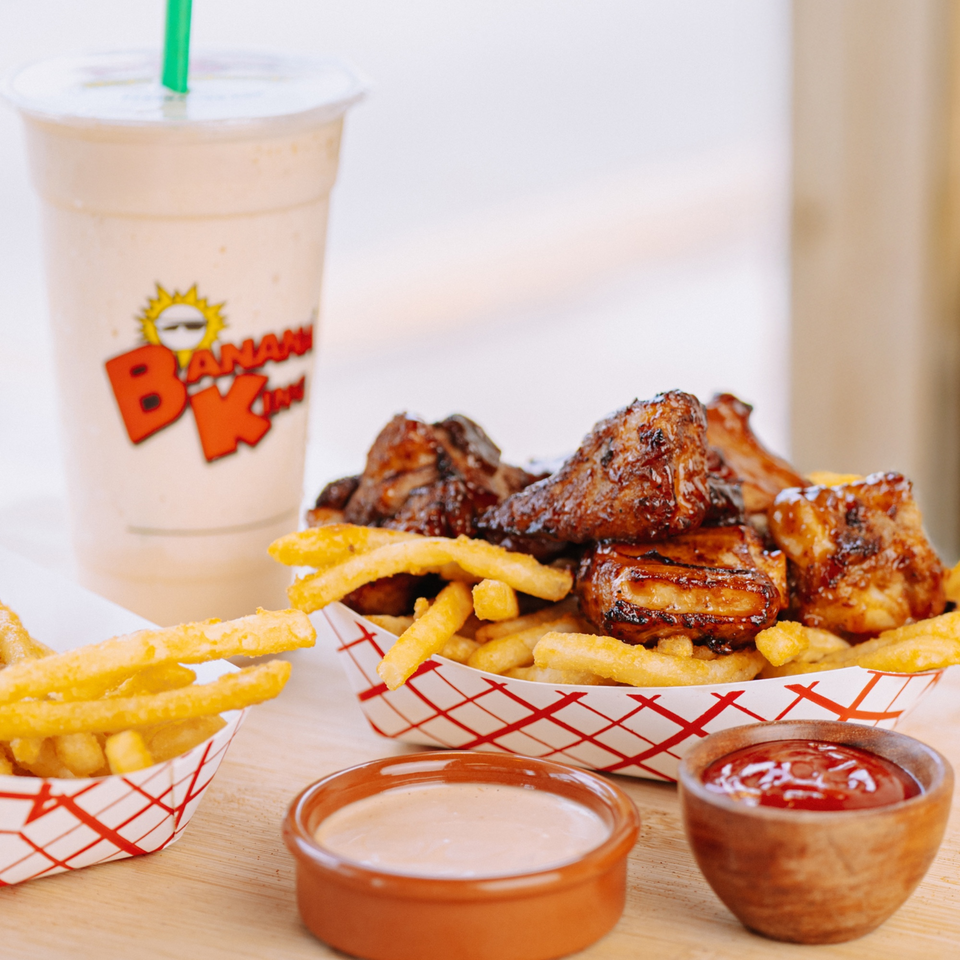 Banana King's BBQ ribs and fries in paper trays, with dipping sauces and a banana milkshake.