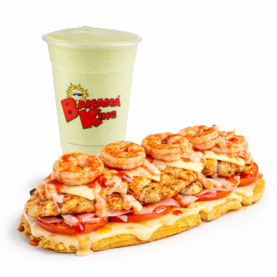 Loaded Banana King sandwich with shrimp, grilled chicken, ham, cheese, tomato, and sauce beside a green smoothie.